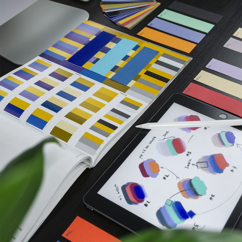 Colour palette book beside a tablet of design sketches on a desk